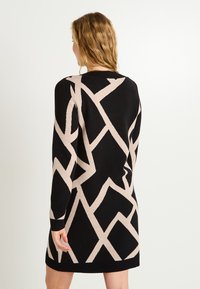 Robe pull noire et beige avec un motif angulaire, des manches longues et un ourlet côtelé, fabriquée en maille douce.