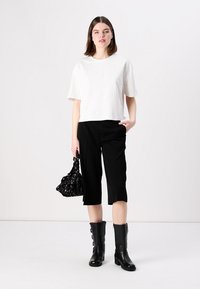 Tricou alb scurt, pantaloni negri cu croi perfect care ajung până la mijlocul gambei și cizme negre până la genunchi. Accesoriile includ o geantă de mână cu model negru.