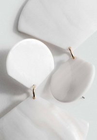 Witte statement oorbellen van gladde hars in verschillende geometrische vormen, met gouden hardware voor een veilige sluiting.
