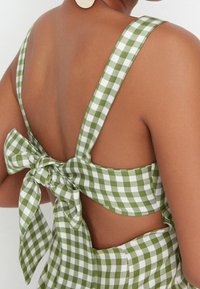 Grünes und weißes Gingham-Kleid mit breiten Trägern und einer Schleifen-Detaillierung im Rücken. Verfügt über einen Ausschnitt und eine glatte Stofftextur.