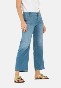 Lichtblauwe wijde spijkerbroek van denim met een vervaagde afwerking, met voorzakken en een knoopsluiting. Gepaard met gouden sandalen.