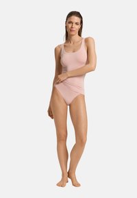 Body rosa chiaro con scollatura a barca e spalline larghe, caratterizzato da una texture liscia e un design aderente, completato da una gamba alta.