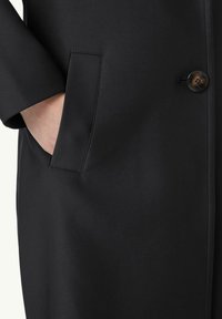 Cappotto nero con un tessuto liscio e texturizzato, chiusura con un solo bottone e tasche laterali con dettagli di cucitura puliti.