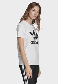 Witte katoenen t-shirt met een groot zwart Adidas-logo met drie strepen boven de merknaam, korte mouwen en een ronde hals.