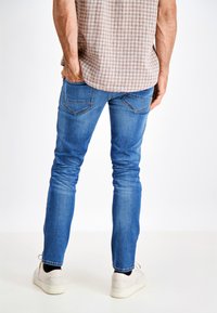 Niebieskie dżinsy slim-fit z wyblakłym odcieniem, pięcioma kieszeniami i kontrastowym przeszyciem, uzupełnione o koszulę w kratę i jasne trampki.