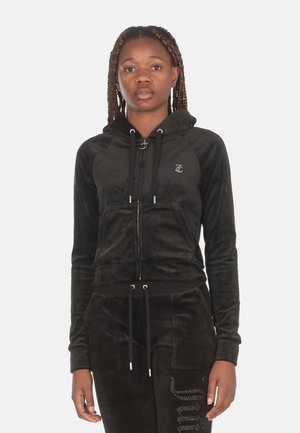 Giacca con cappuccio in velluto nero, con zip frontale, coulisse e un piccolo logo. Abbinata a pantaloni coordinati con un design testurizzato.
