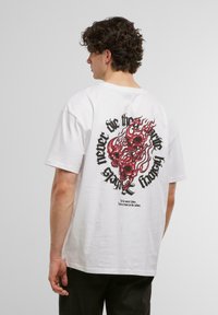 White cotton t-shirt with a round neckline and short sleeves. Features a graphic of red flames and skulls on the back. Black lettering included.