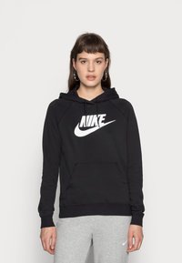 Felpa nera con cappuccio e logo Nike bianco, tasca a marsupio, polsini e fondo a costine, realizzata in un morbido tessuto testurizzato. Abbinata a pantaloni da tuta grigi.