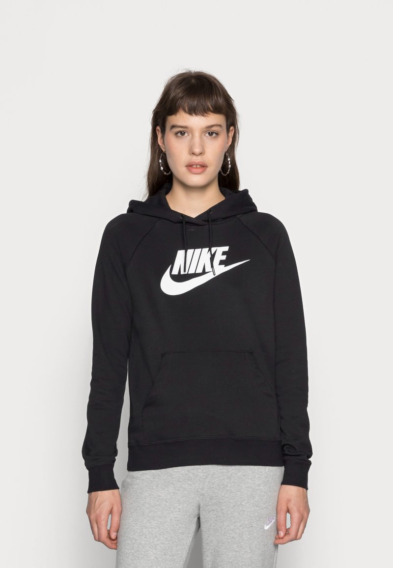 Felpa nera con cappuccio e logo Nike bianco, tasca a marsupio, polsini e fondo a costine, realizzata in un morbido tessuto testurizzato. Abbinata a pantaloni da tuta grigi.