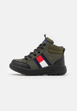 Basket montante enfant en vert olive avec semelle noire, lacets noirs, cheville rembourrée et détail de bande latérale rouge, blanche et marine.