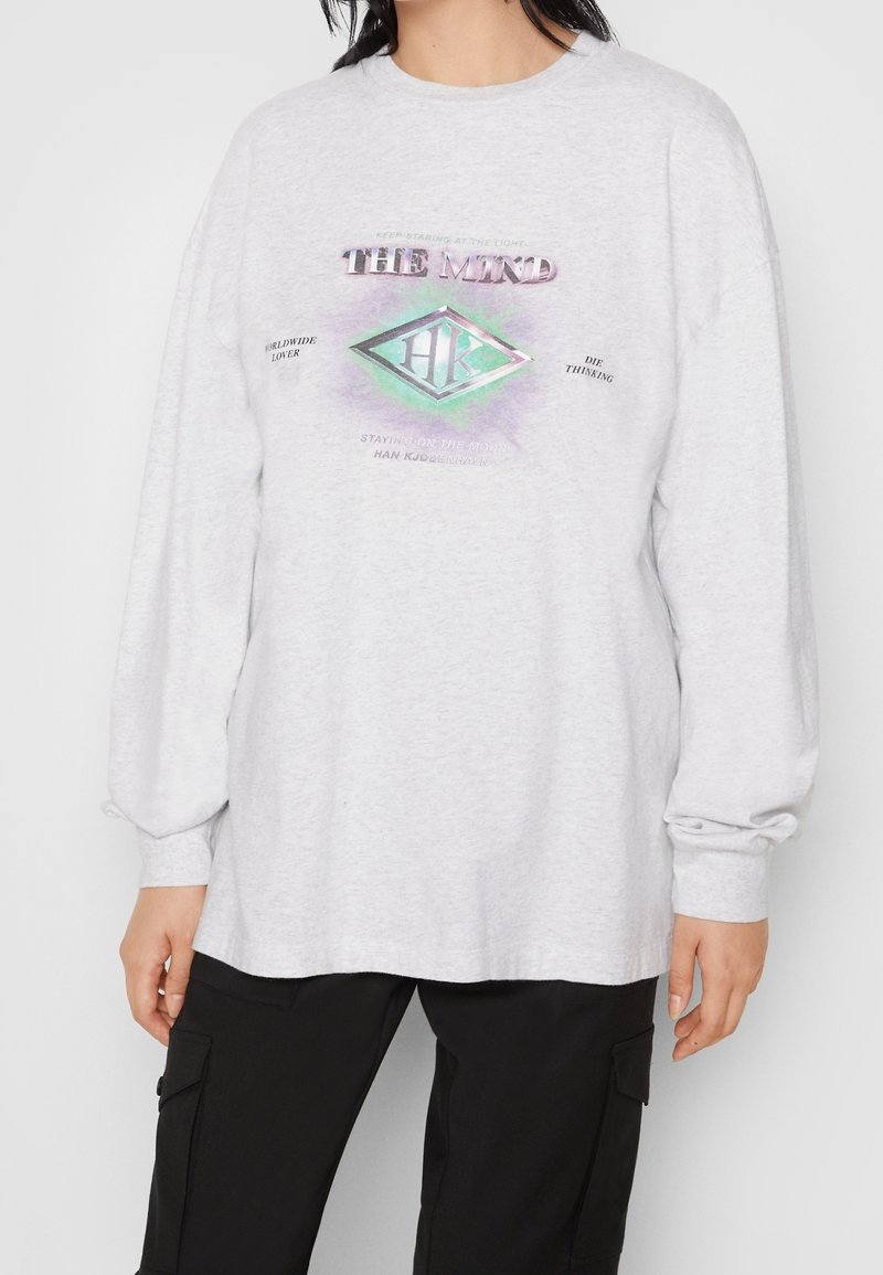 Grå långärmad t-shirt med en lös passform. Har en flerfärgad grafisk design i mitten och text runtom. Mjuk bomullstextur.