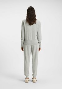 Light grey loungewear set comprising a knitted sweater and pants. Ribbed cuffs and waistband, relaxed fit, soft texture, paired with beige shoes.