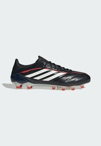 Chaussure de football noire avec une tige texturée, comportant trois bandes blanches et des accents rouges. Semelle extérieure transparente avec des crampons rouges contrastants.
