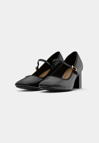 Chaussures Mary Jane en cuir noir avec talons blocs et brides ajustables avec petites boucles dorées.
