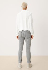 Camicia bianca stropicciata, jeans in denim grigi con risvolti sulle caviglie e sneakers chiare. La vista posteriore evidenzia i dettagli delle tasche e la vestibilità.