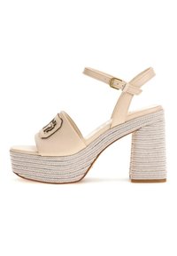 Sandali platform beige con una larga fascia curva e una fibbia ampia. Il tacco intrecciato e testurizzato presenta un spesso motivo a spina di pesce e una suola piatta.