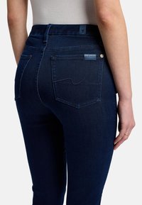 Jeans de mezclilla azul oscuro con una cintura de altura media, bolsillos traseros visibles y detalles de costura en contraste. Textura suave y diseño ajustado.