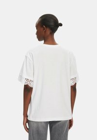 T-shirt bianco in cotone a maniche corte con delicata rifinitura in pizzo. La vista sul retro mostra un taglio morbido e un design a collo rotondo.