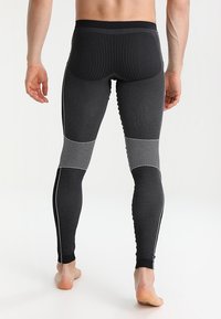 Mallas deportivas negras con textura acanalada, detalles de malla en la pantorrilla y rayas laterales blancas. El material parece elástico y ajustado.