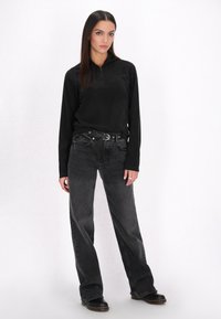 Zwarte zip-up met lange mouwen, gecombineerd met losse, vervaagde zwarte jeans. De outfit heeft een aansluitende pasvorm en gestructureerde materialen. Zwarte laarzen maken de look compleet.