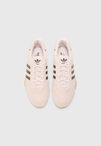 Lyserøde ruskinds sneakers med tre sorte striber, hvide snørebånd og gummisål. Indvendigt er de polstret for komfort, og der er brandmærke på tungen.