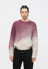 Sweter w odcieniach bordo i kremu z teksturowanym wykończeniem, długimi rękawami i okrągłym dekoltem. Nosi się go z czarnymi spodniami.