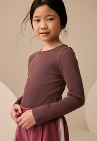 Długi rękaw, ribbed top w głębokiej mauve, połączony z miękkimi, różowymi spodniami ze sznurkiem w talii, ozdobionymi bocznymi paskami. Gładka tekstura, dopasowany krój.