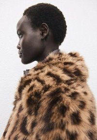 Cappotto in pelliccia sintetica marrone con un motivo leopardato, che mette in mostra una texture morbida e un colletto strutturato, indossato da un modello di profilo.