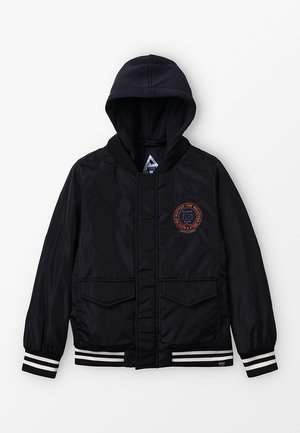 Veste à capuche noire avec poches avant à rabat, poignets et ourlet rayés, et un écusson logo rond sur la poitrine gauche portant la mention "NO MATTER THE WEATHER.".
