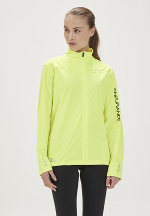 Fluorescerende gele sportjack met hoge kraag, rits aan de voorkant en gestructureerde zijkanten. Voorzien van logo's in zwart en zilveren accenten.