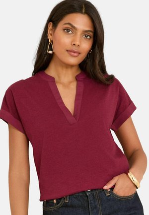 Haut bordeaux à manches courtes avec un design en V, en tissu texturé, avec des poignets roulés et une coupe droite, associé à un jean foncé.