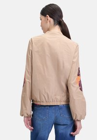 Tan bomberjack met een elastische tailleband, met levendige bloemenborduursels op de mouwen. Glad, lichtgewicht stof met een cropped ontwerp.