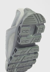 Suola di scarpe sportive grigia con gomma testurizzata per una presa ottimale, tallone rinforzato e dettagli in rete. Design curvo con elementi di ventilazione.