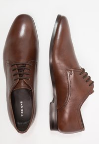 Bruna läderskor med slät yta, rund tå och snörning. Låg klack med subtila sömnadsdetaljer. Märket synligt inuti.