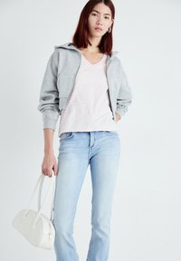 Gray cropped hoodie with a zipper, light pink striped v-neck T-shirt, light blue jeans, and a small white handbag with two handles.