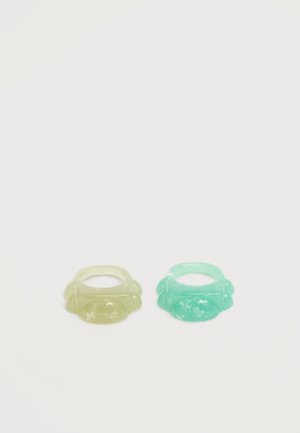 Two translucent rings, one pale yellow and one light turquoise, each with a rounded, decorative band design, on a plain white background.