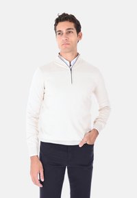 Pullover beige chiaro con colletto a mezza zip, polsini e orlo a coste, abbinato a pantaloni blu scuro. Materiale in maglia morbida, design semplice.