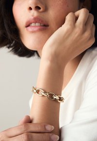 Gold chain bracelet featuring interlocking oval and round links, set against a light background with a focus on smooth texture and shine.