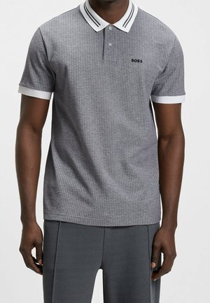 Mann trägt ein grau gemustertes kurzärmeliges Polo mit weißem Kragen und Bündchen, "BOSS" Logo auf der Brust, kombiniert mit passenden grauen Hosen.