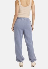 Jasnoniebieskie sportowe spodnie dresowe o miękkiej fakturze, z elastycznym pasem i zwężającymi się mankietami. Połączone z beżowym topem na ramiączkach i beżowymi trampkami.