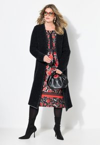 Mustat neulottu pitkä neuletakki, jossa on valkoista tikkauksia, päällä punainen kukkamekko. Asusteina musta käsilaukku ja mustat korkokengät.