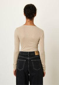 Long-sleeve, fitted top in light beige, paired with high-waisted, dark denim jeans featuring a patch label and contrasting stitching details.