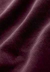 Tissu texturat de culoare violetă cu un model cu dungi verticale, prezentând unduiri moi ale suprafeței și o variație bogată de culori în lumină.
