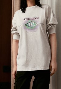 Ljust grå överdimensionerad t-shirt i bomull med grafiskt tryck av text och former i grönt och lila, rund halsringning och uppkavlade ärmar.