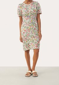 Robe florale midi avec une palette de couleurs vert, blanc et rose, à manches bouffantes courtes et silhouette ajustée. Associée à des sandales légères.