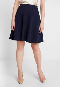 Marinblå veckad kjol i texturerad tyg, knälång, med ett åtsittande midjeband och mjukt fall. Matchad med beiga högklackade skor.