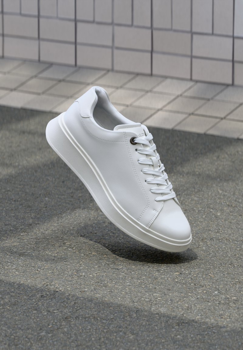 Adidași din piele alba cu o suprafață netedă, vârf rotund, șireturi plate și talpă de cauciuc texturată, suspendați pe un fundal gri.