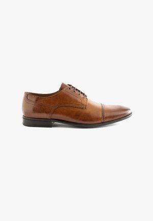 Scarpa da dress in pelle marrone con punta arrotondata, dettagli cuciti e una suola in gomma nera testurizzata bassa. Caratterizzata da allacciatura con cinque occhielli.