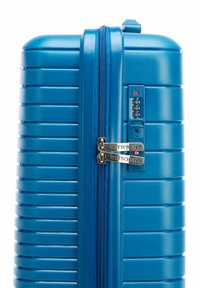 Blue hardshell suitcase with textured finish, horizontal ridges, dual metal zippers, combination lock, and brand logo prominently displayed.