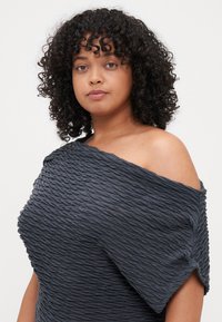 Tumši pelēks off-the-shoulder tops, izgatavots no faktūras, savākta auduma. Raksturīga brīva siluets un vaļīgas piedurknes ērtai nēsāšanai.